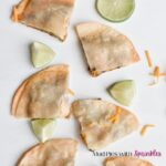 Black Bean Quesadilla Recipe for for Kids with tortilla wedges scattered along a white surface with halved limes and sprinkled cheese.
