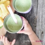 A child grabs a stainless steel cup filled with green pineapple spinach smoothie for kids.