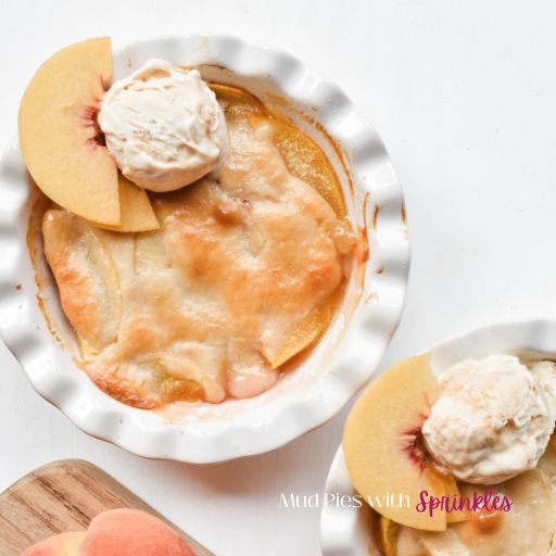 Easy mini peach cobbler baked into two 6-ounce ramekins arranged on a white table with freshly sliced peaches and a scoop of vanilla ice cream with homemade caramel syrup.