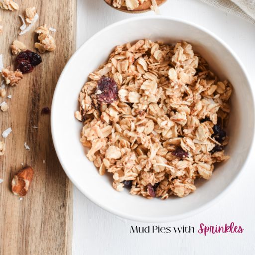 Coconut Almond Granola mixed into a white ceramic bowl with ingredients arranged on a wooden serving board.